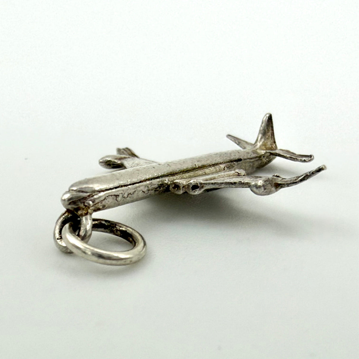 A small silver airplane charm pendant with a split ring, shown on a plain light gray background.
