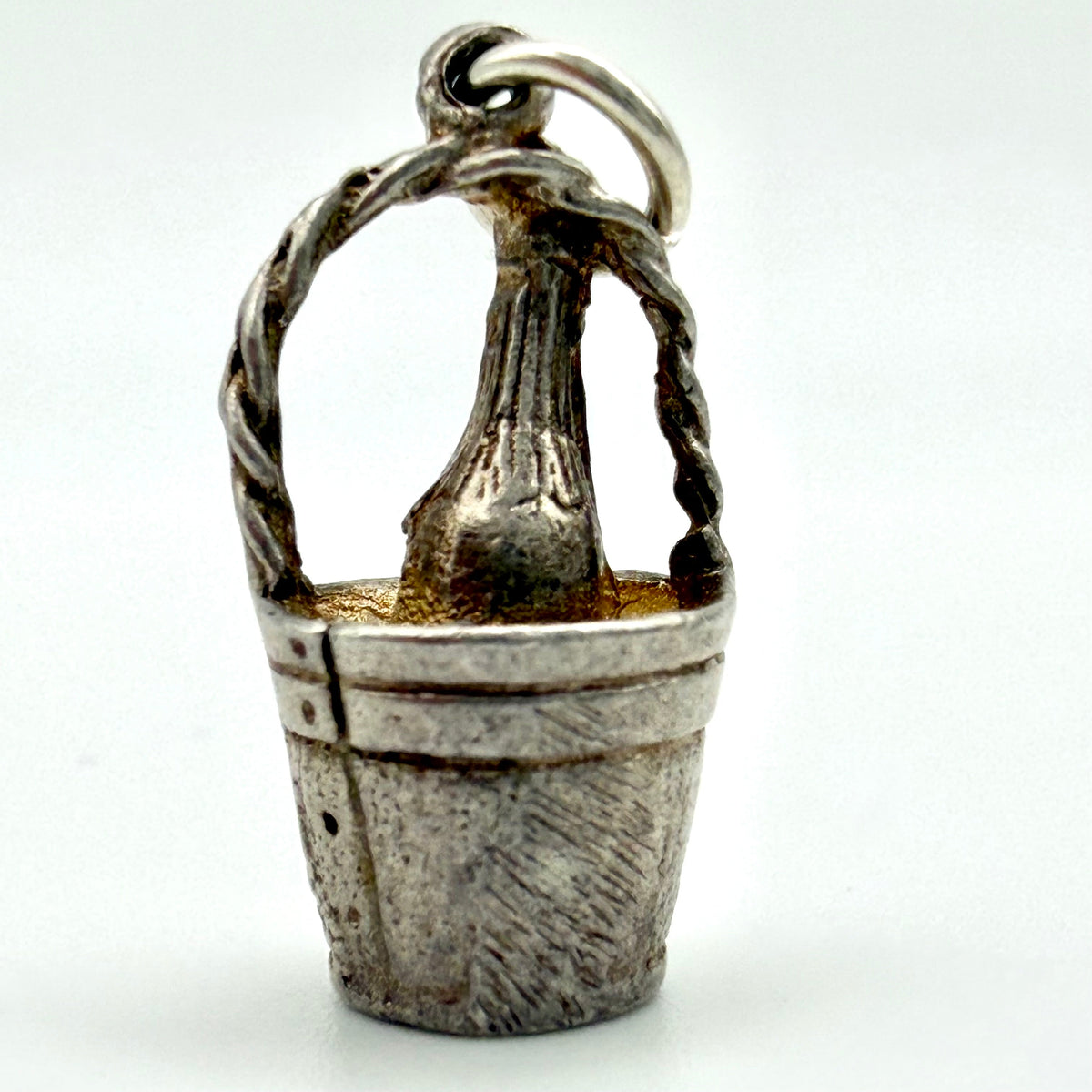 A sterling silver pendant shaped like a rustic bucket with a twisted handle and a central textured vertical element, shown on a plain light background.